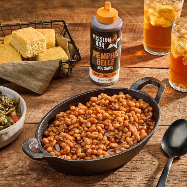 A bottle of Memphis Belle BBQ Sauce on a table with a dish of Baked Beans